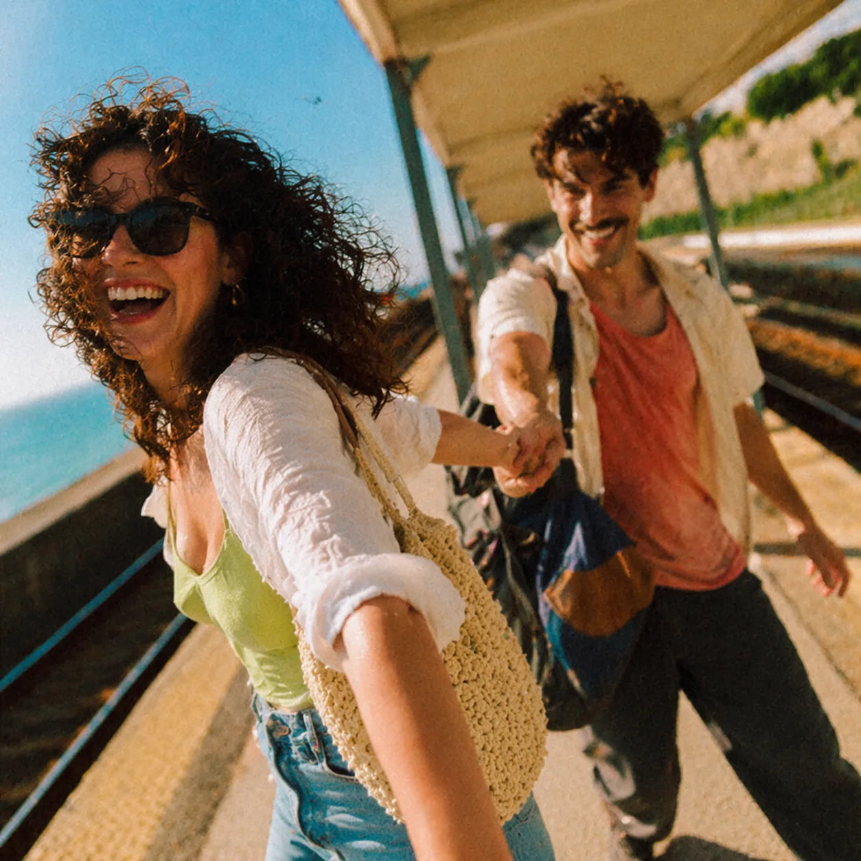 Two friends laughing together on a sunny coastal train platform